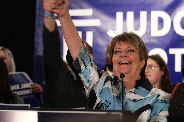 Judge Janet Protasiewicz waves from a podium and smiles.