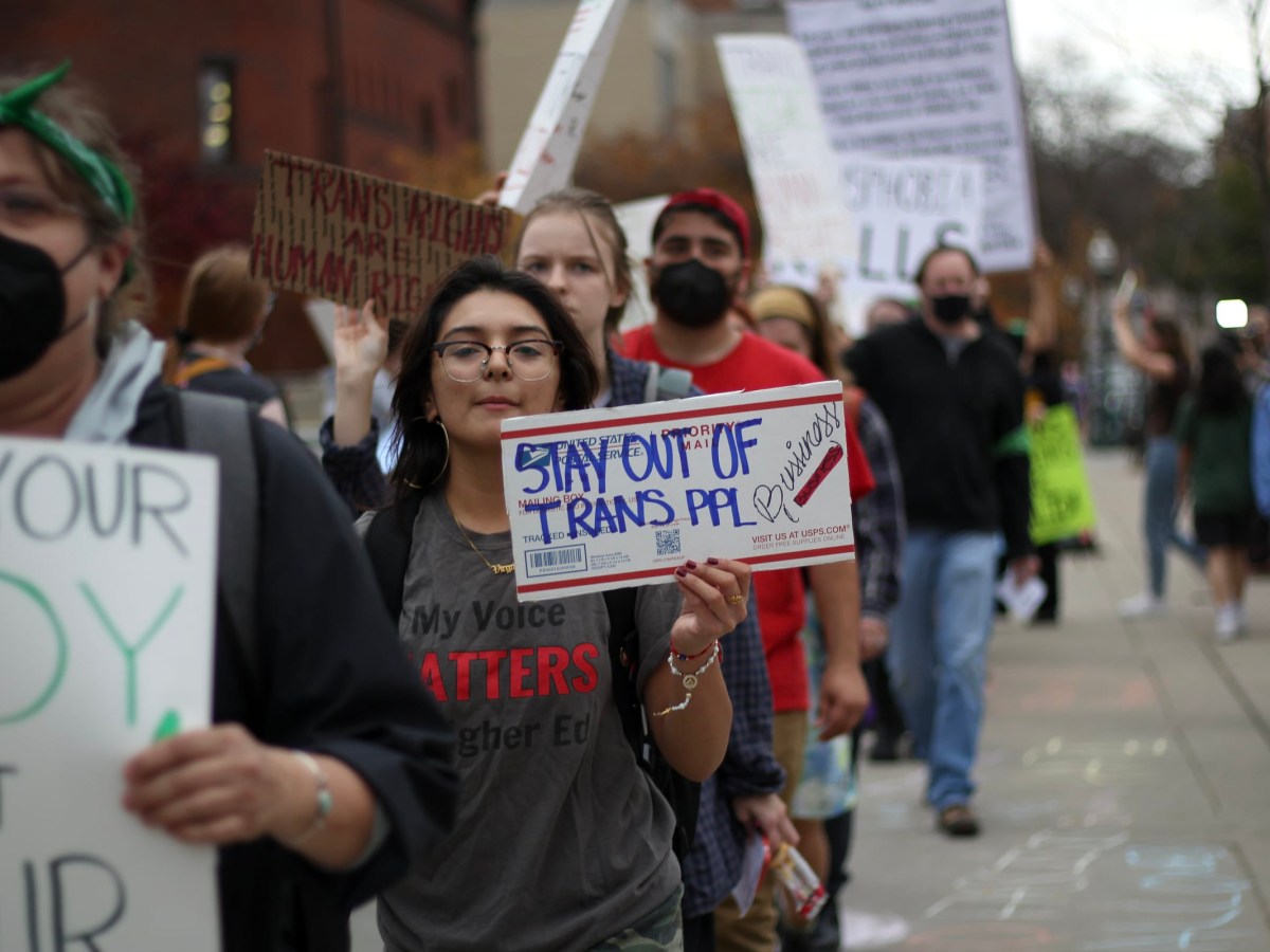 A protestor holds a sign that reads "Stay out of trans people's business."